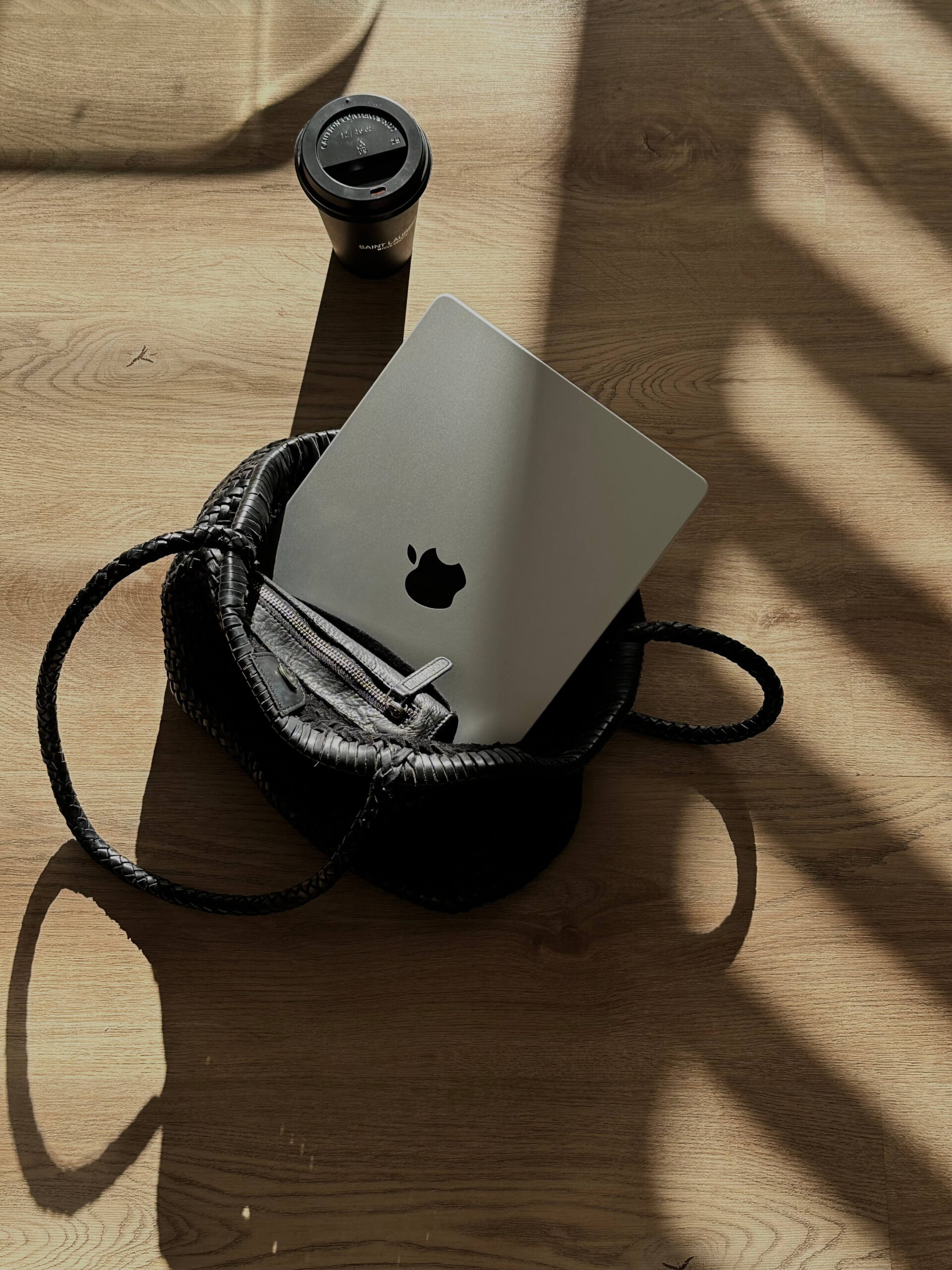 Laptop in a purse on the floor near a cup of coffee.